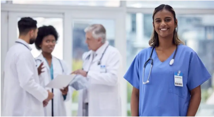 Infirmière souriante au premier plan dans un hôpital, avec une équipe de professionnels de santé en arrière-plan.