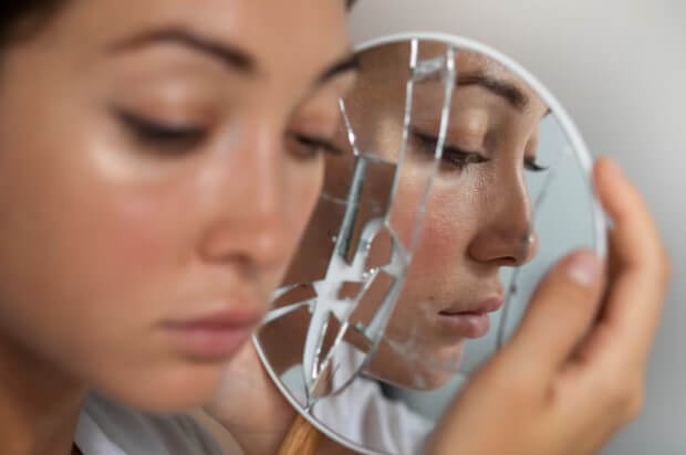 Femme regardant son reflet dans un miroir, le visage marqué par une imperfection cutanée