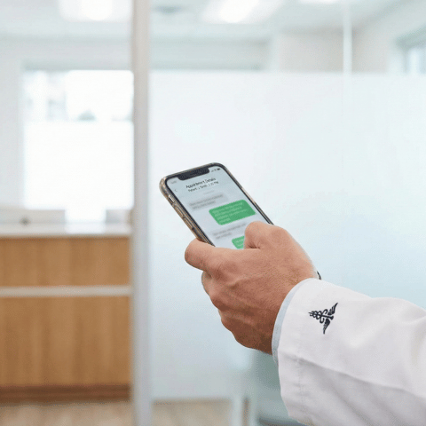 Médecin consultant un smartphone pour la gestion des rendez-vous et le suivi des patients via WhatsApp.